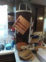 White metal 7-hook pot rack hanging, wooden shelving unit with angled slots, metal pig decor figurine, and several wooden cutting boards on counter.