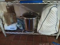 Three items displayed on metal shelving: food processor, stock pot, mixer cover