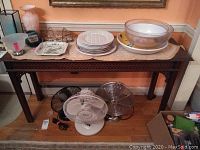 Console table with various household items placed on top and some fans underneath, showcasing the full length and height of the table.