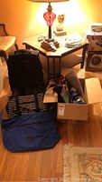 Photo showing black leather rolling bag, striped bag, and box of multiple beach bags on wood floor next to furniture.