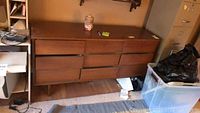 Full view of wooden mid-century modern dresser with nine drawers and wear on surface, no contents included.