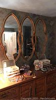 Three-panel wall mirror with gold-tone carved frames above a dresser with assorted items.