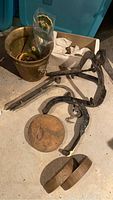 Overview photo showing metal bucket, iron hooks, copper wedges, wooden blocks on concrete floor with visible dust and wear