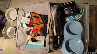 Wide view of pet bed with various pet supplies including bowls, life preserver vest, toys, and leashes spread on and around the bed