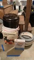 Weight Watchers electronic food scale sealed box, Ronco and Nesco food dehydrators stacked on a box in basement area.