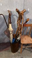 Walking sticks and umbrellas in metal stand beside wooden chair