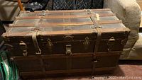Front view of the antique trunk showing leather straps, brass locks, and wooden slats.