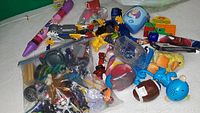 Photo showing a large assortment of small toys including plastic figurines, a toy football, a blue toy with a face, and miscellaneous novelty items in various colors.