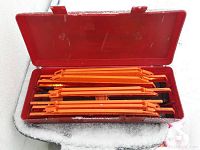Photo of three folded orange road safety triangles placed inside a red plastic case with the lid open, shown on a snowy surface.