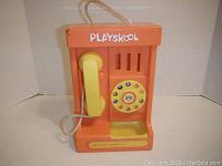 Front view of orange Playskool toy telephone with attached yellow handset and rotary dial.