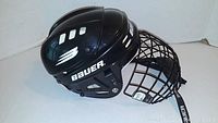 Side view of black Bauer hockey helmet with attached metal cage face guard, showing Bauer logo and ventilation slots.