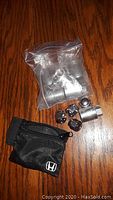 Clear view of all items included: four lug lock nuts, key tool sealed in plastic bag, and black Honda pouch.