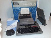 Sears Type-O-Graph typing machine with box, manual, power cord, and cover displayed, all contents visible.