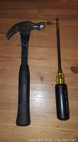 Claw hammer and large screwdriver placed side by side on a wooden surface