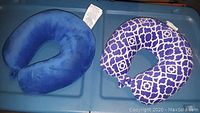 Photo showing two travel neck pillows on a plastic container lid, one solid blue and the other blue and white patterned.