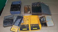 Six sets of assorted drill bits in various cases including DeWalt branded yellow plastic cases and metal storage boxes.