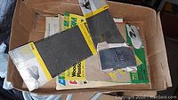 Photo of assorted new sandpaper sheets in packaging showing different grit levels and labels.