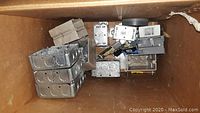 Photo showing a cardboard box containing multiple chrome electrical boxes, metal outlets, switches, and mounting hardware all stacked inside.