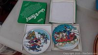 Two Walt Disney collector plates in white boxes shown on a table.
