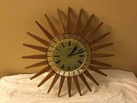 Front angle photo of the starburst style wall clock showing wooden rays and circular clock face.