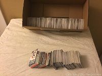 View of large quantity of hockey cards stacked and placed in cardboard box and on table.