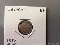 Photo of 1913 Canadian small nickel 5 cent coin in cardboard holder with handwritten notes indicating year, condition, and denomination.
