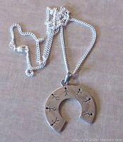 Front view of the silver pendant and chain showing modernist half circle pendant with stick figure cutouts