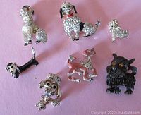 Seven vintage dog brooches with various dog breeds and enamel wear laid out on pink background.