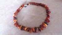 Full view of amber chip bead necklace arranged in a circle on fabric background, showing color variation and chip shapes.