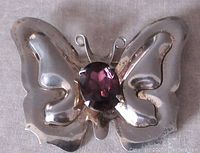 Front view of the butterfly brooch showing the large oval facetted purple glass stone and silver wings.