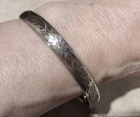 Close-up of the vintage sterling silver bangle bracelet with floral engraving on wrist, showing design detail and clasp.