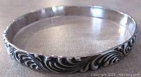 Side angled view showing the embossed swirling pattern design with oxidized background on a sterling silver child's bangle.