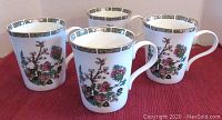 Four Crown Trent Indian Tree pattern mugs sitting on a red cloth, showing the floral design and gold trim on the outside of each mug.