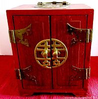 Front view of vintage dark wood jewelry cabinet with two doors, brass hinges, and large round brass ornamental clasp.