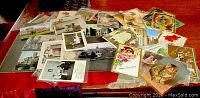 Spread of 37 antique postcards and some greeting cards arranged on a table, showing a variety of subjects including children, cats, greetings and themed illustrations.