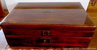Closed view of wood storage box with waxed finish, brass plaque on top, and front keyhole.