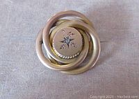 Front view of an antique Victorian 10K gold love knot pin. Central diamond set in engraved floral motif. Matte finish gold knot design approximately 1 inch in diameter.
