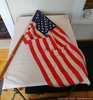The full view of the American flag attached to a wooden pole, draped over a table.