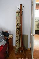 Photo showing vintage wooden coat tree standing beside rolled-up area rug.