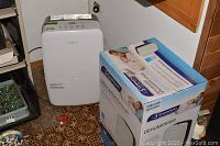 White Garrison dehumidifier plugged into wall outlet; unit standing on patterned floor next to shelving unit.