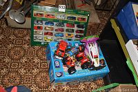 Photo showing the RC hovercraft on top of its blue box and the green sealed collector toy car set behind it on a patterned carpet.