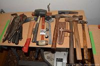 Top view of lot on table showing diverse hand tools including hammers, mallets, hatchets, pry bars, wrenches, and brass plumb bob.