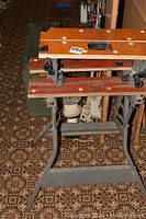 Full view of foldable Workmate bench with metal frame, wooden top with clamp handles and round holes