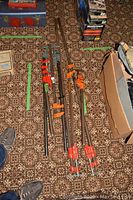 Overview of eight steel bar clamps laid out on patterned carpet, showing varying bar lengths and cast iron clamp heads in red and orange