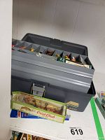 Grey tackle box open showing multiple compartments filled with lures and fishing accessories