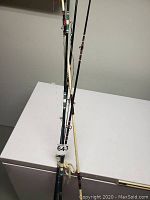 A group of three deep water fishing rods standing upright showing their length and build.