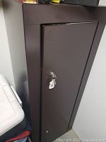 Front view of brown metal gun cabinet with keys in lock