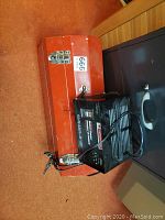 Red metal chest with Motomaster charger on carpeted floor