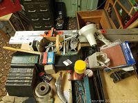 Overview image showing various tools, books, and hardware items arranged on a table including a box of nails, gasket sets, a vise, and various hand tools.