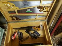 Wooden case interior showing three long hand saws secured to lid and six hand planes along bottom